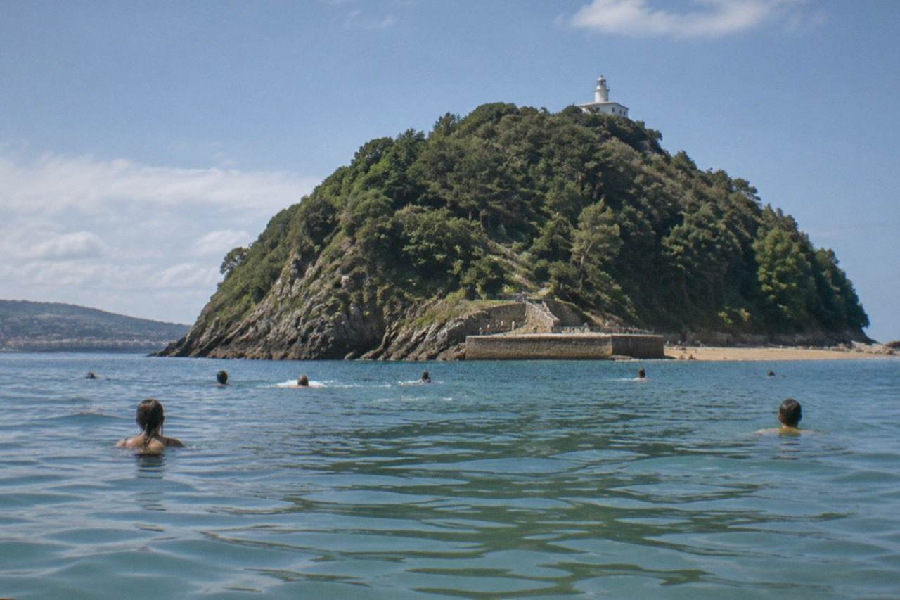 Swimmers in calm water at La Concha beach with Santa Clara island behind them