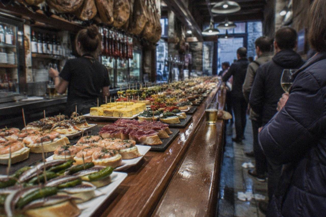 A pintxo bar counter in the Old Town of San Sebastián with a bartender serving guests