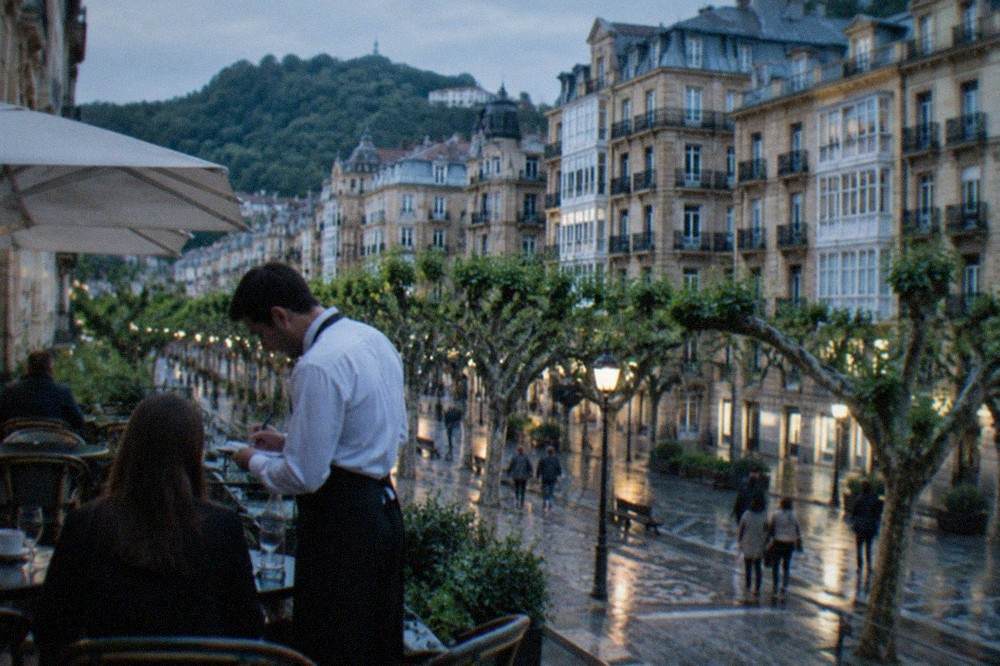 A waiter writing an order at an outdoor cafe table on a tree-lined street