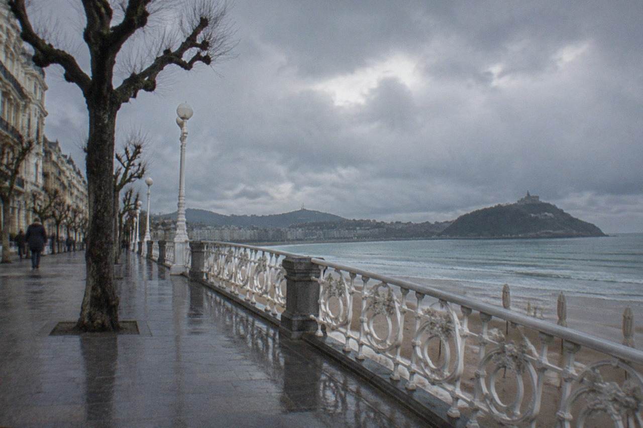 Rain clouds over La Concha bay in San Sebastián with wet sand and empty parasols along the promenade