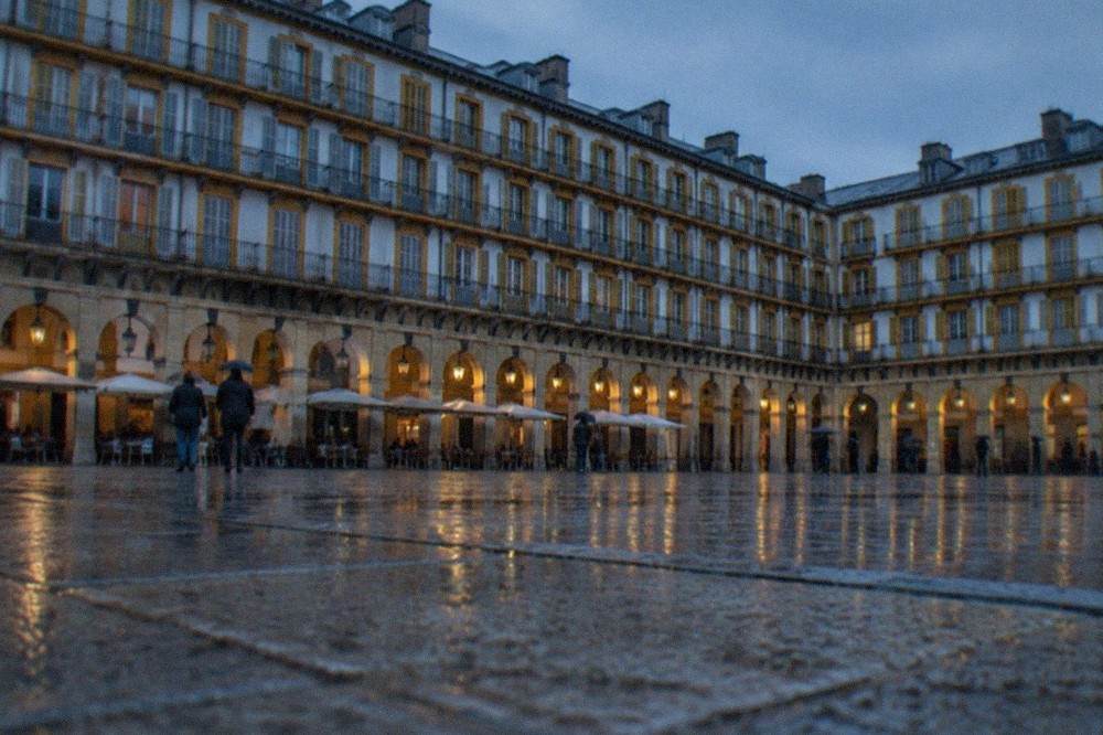 People sheltering under the arcades of Plaza de la Constitucion in San Sebastián's Old Town on a drizzly day