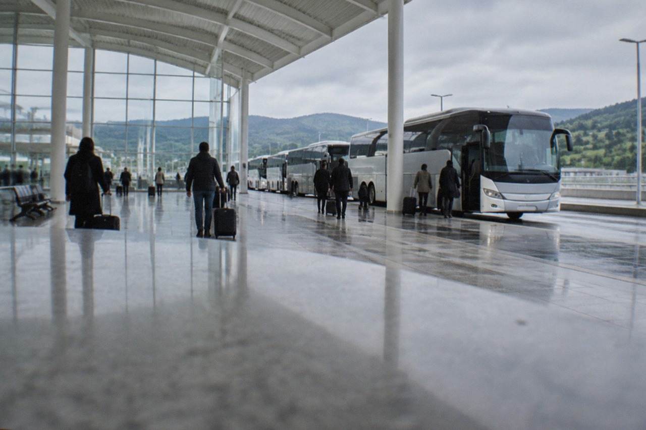 Coaches lined up at an airport terminal curb under a grey sky