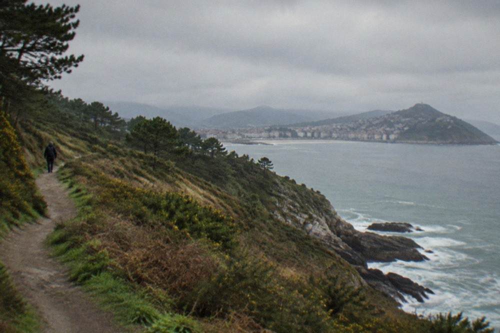 A coastal trail winding above rocky cliffs with a small fishing town in the distance