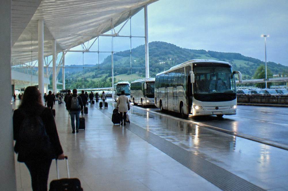 A regional bus parked at an airport curb beside a row of coaches