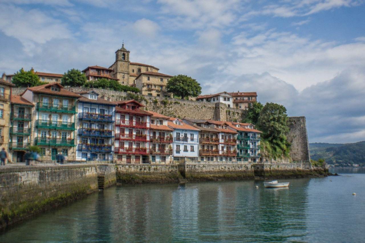 Colourful wooden houses and a stone wall above the waterfront in Hondarribia on a bright day