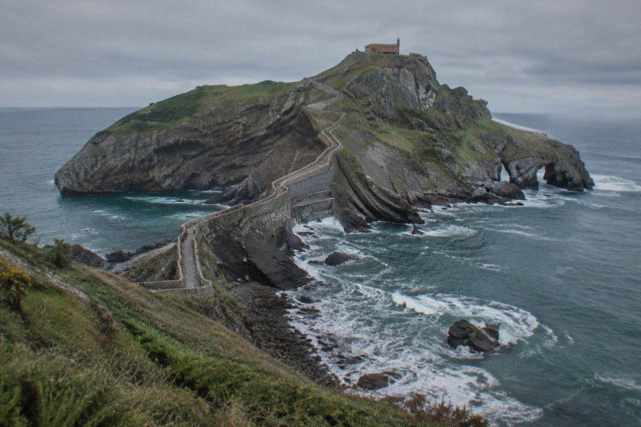 The rocky islet of Gaztelugatxe with its stone causeway winding down to the sea under a grey northern Spanish sky