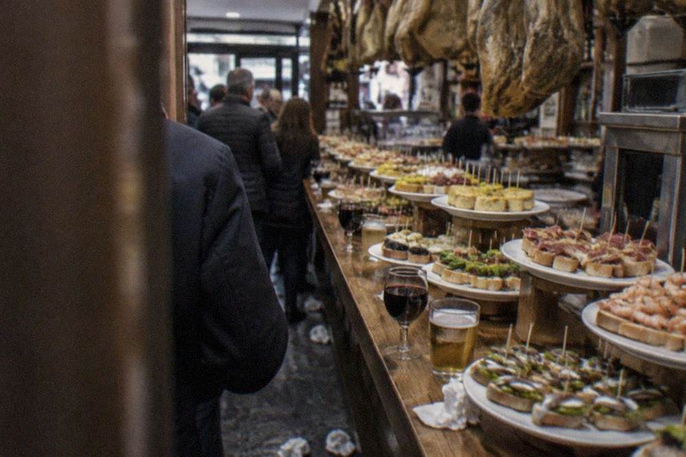A pintxo bar counter in the San Sebastián Old Town, with skewered bites arranged on plates along the bar top