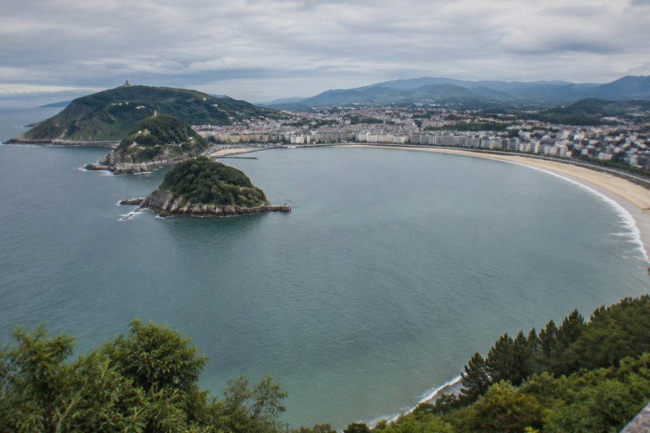 The curve of La Concha bay in San Sebastián seen from above, with the beach, island and green hills