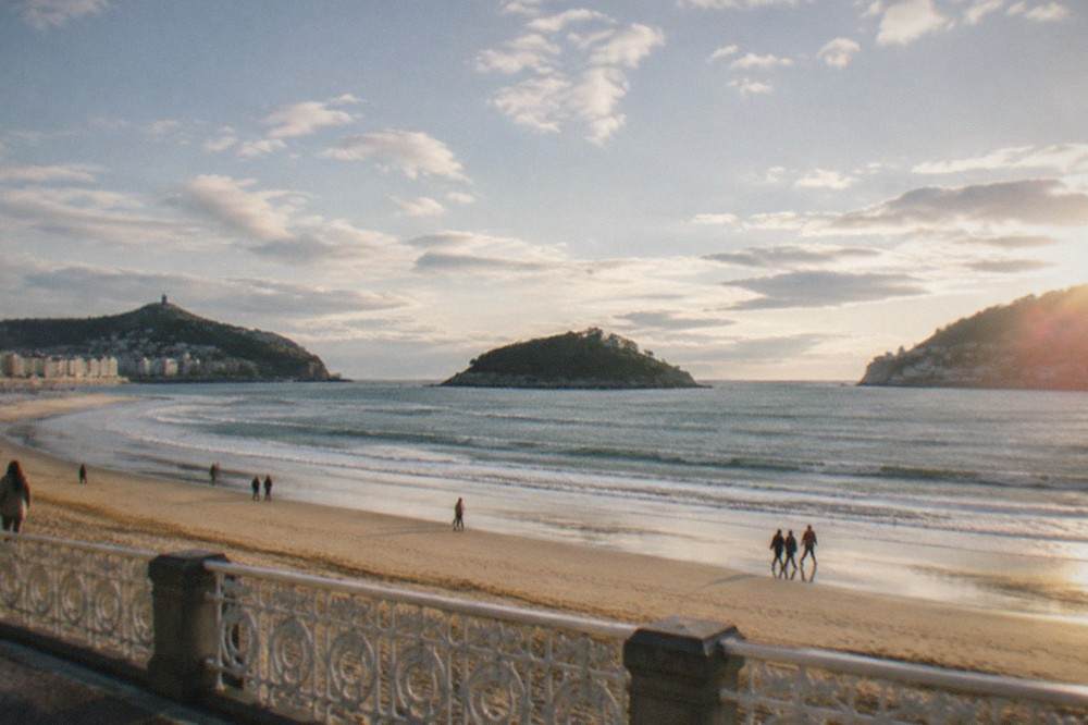 People walking on the sandy curve of La Concha beach with the island and hills behind