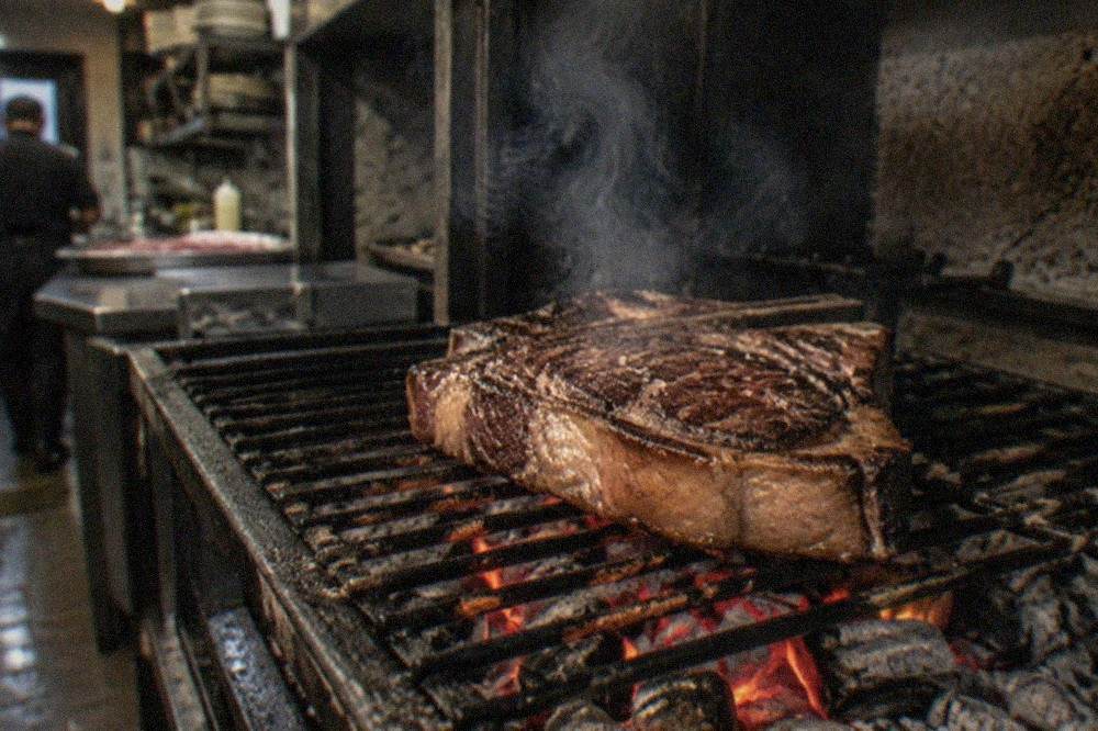 A thick ribeye steak grilling over charcoal in a Basque restaurant kitchen