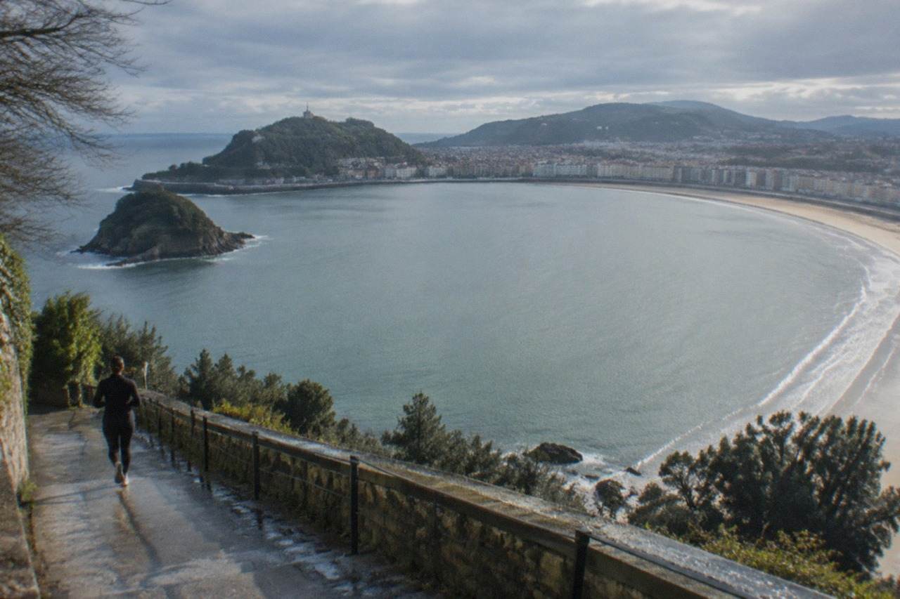 The curved sandy bay of La Concha in San Sebastián seen from above, with the island and green hills behind the water