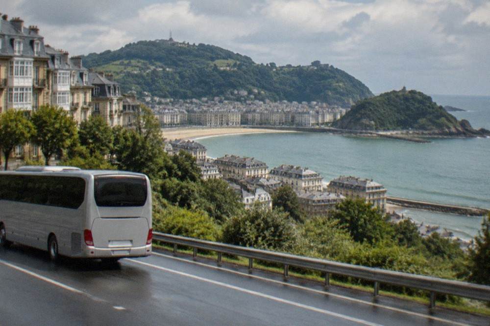 An intercity coach driving along a motorway with green Basque hills and the sea in the distance