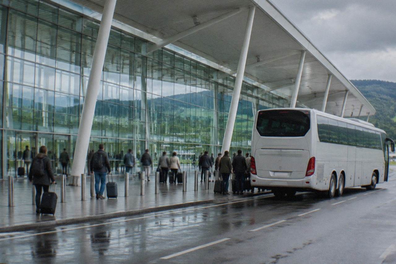 A long-distance coach parked at an airport terminal curb under a grey northern Spanish sky
