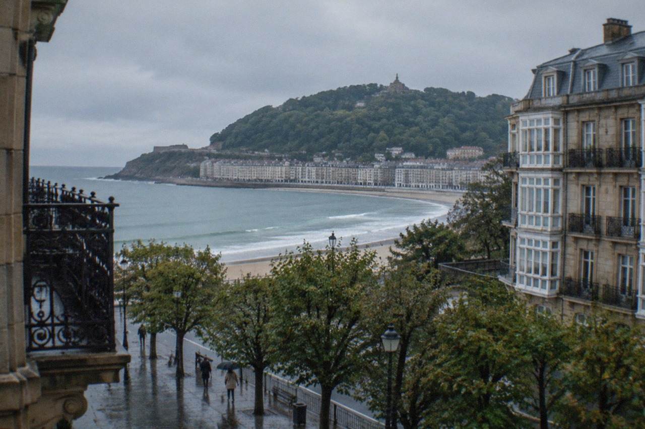 A large statue of Christ standing on a stone platform above the bay of San Sebastián, with the sea and city below