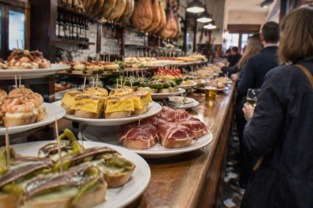 A pintxo bar counter in the Old Town of San Sebastián, with small topped bread slices arranged on plates under the lights