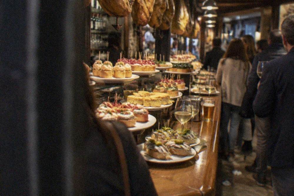 A counter of pintxo bars in the San Sebastián Old Town at evening, with glasses of white wine on the bar
