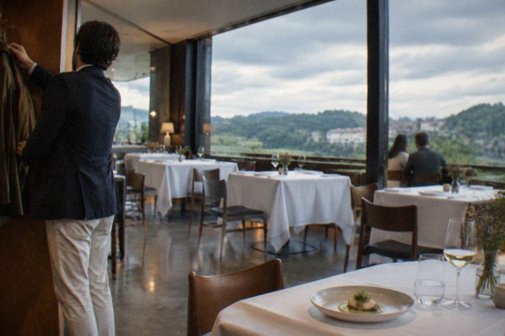 A diner in a smart-casual jacket hanging a coat at a restaurant cloakroom before dinner