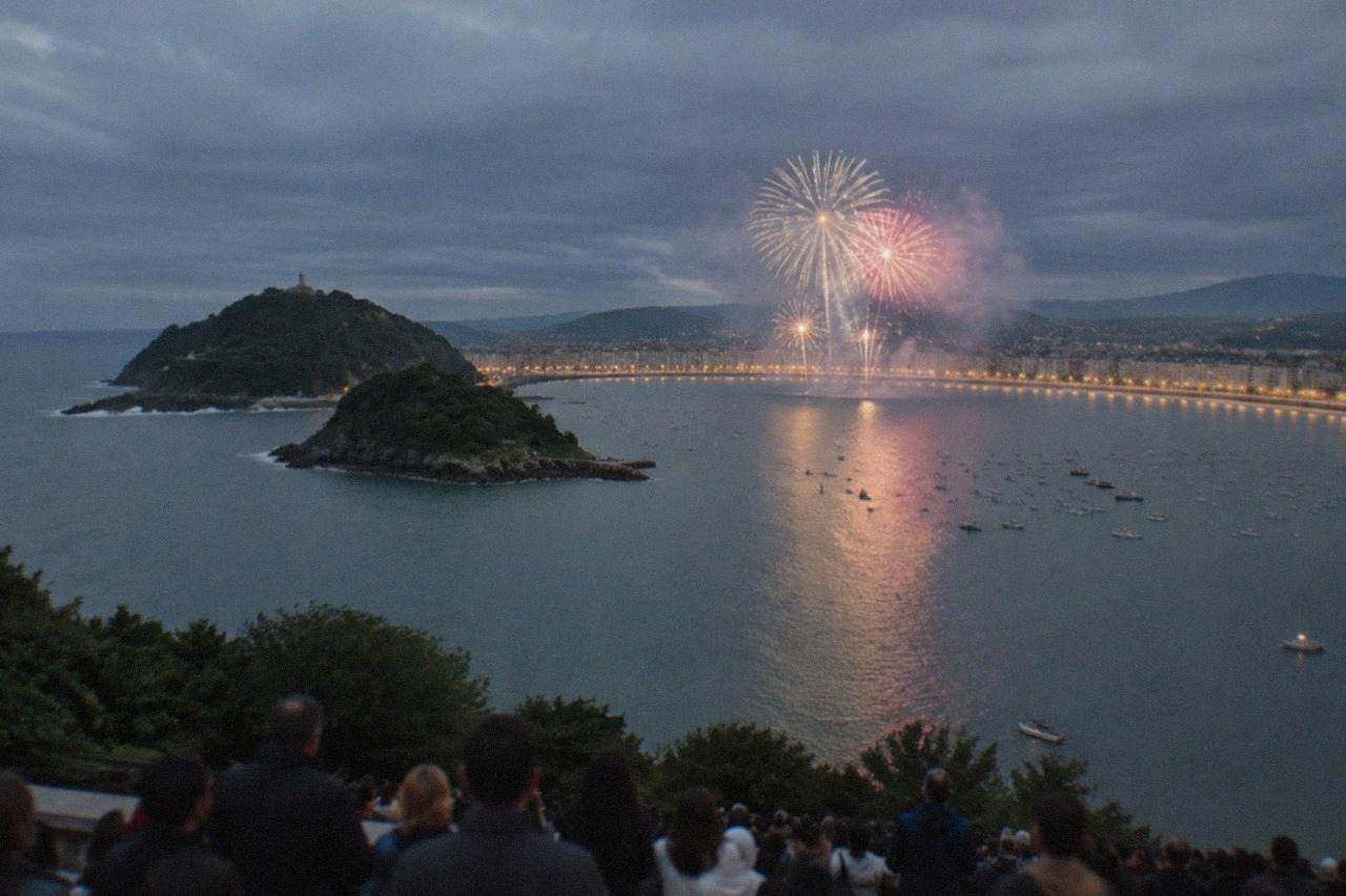Crowds watching a fireworks display over La Concha bay in San Sebastián at night