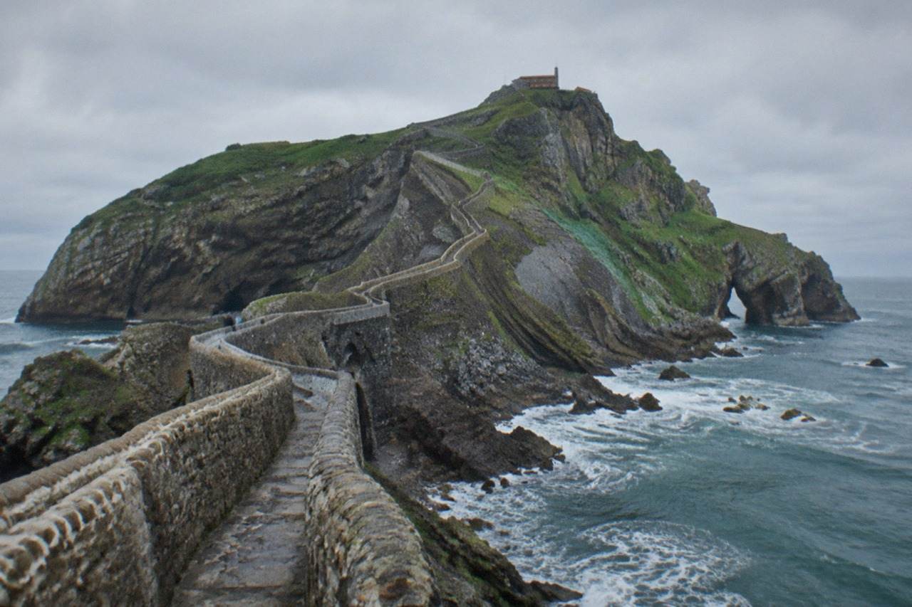 A rocky islet off the green Basque coast connected to the mainland by a narrow stone bridge and a long stairway