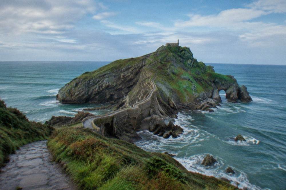 A small stone hermitage on the summit of a coastal islet, seen from the cliff path above the sea