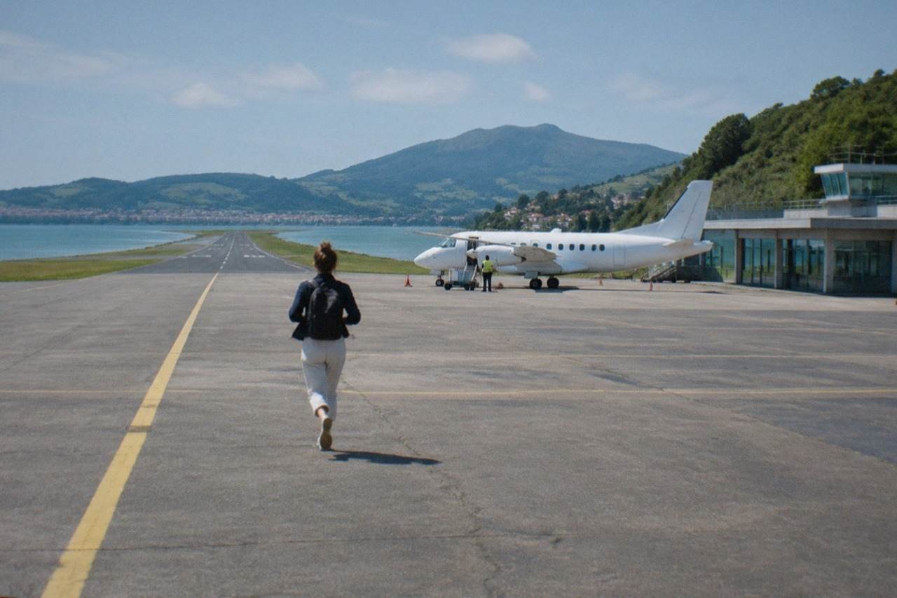 A small regional airport terminal beside a green hillside with a plane at the stand