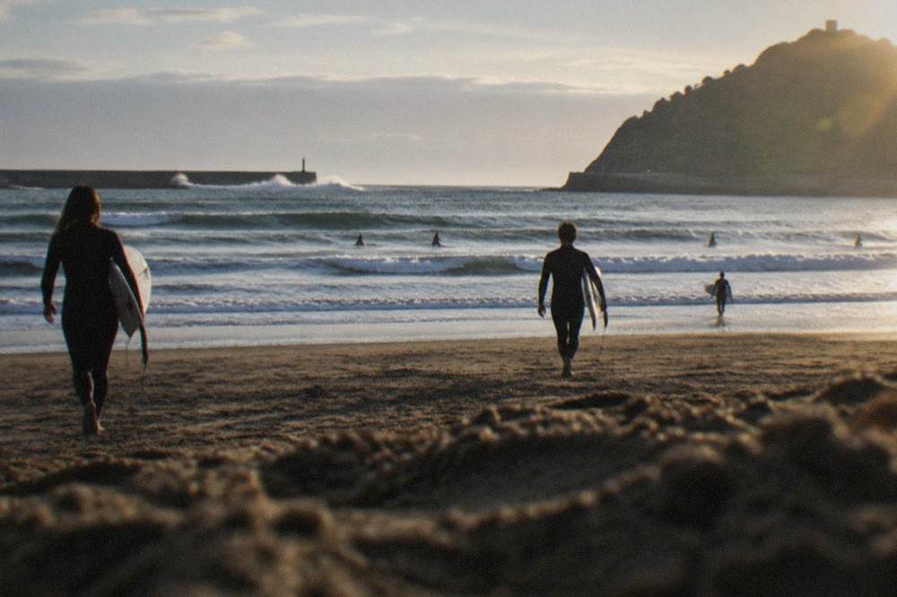 Waves breaking on the open sandy stretch of Zurriola beach with surfers in the water