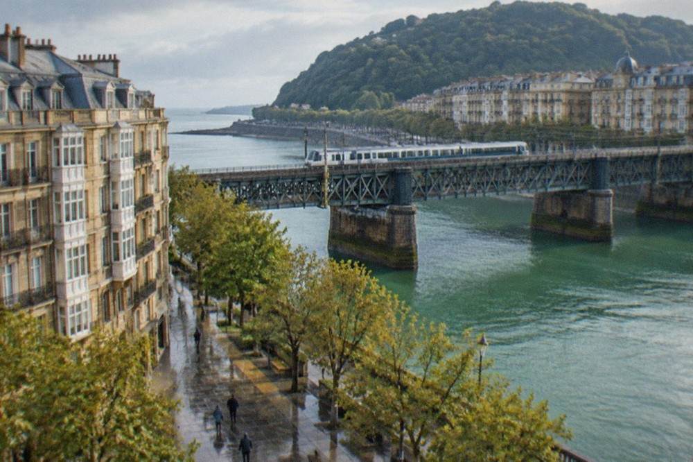 A regional train crossing an iron bridge over a green river estuary in the Basque Country