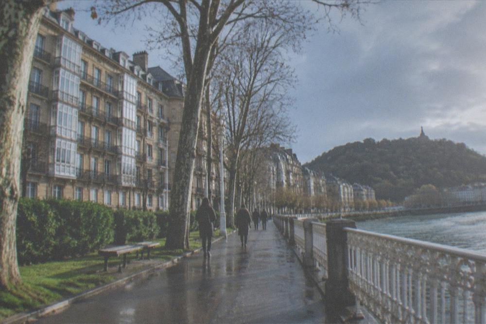 People walking a tree-lined path beside the Urumea river toward the bay
