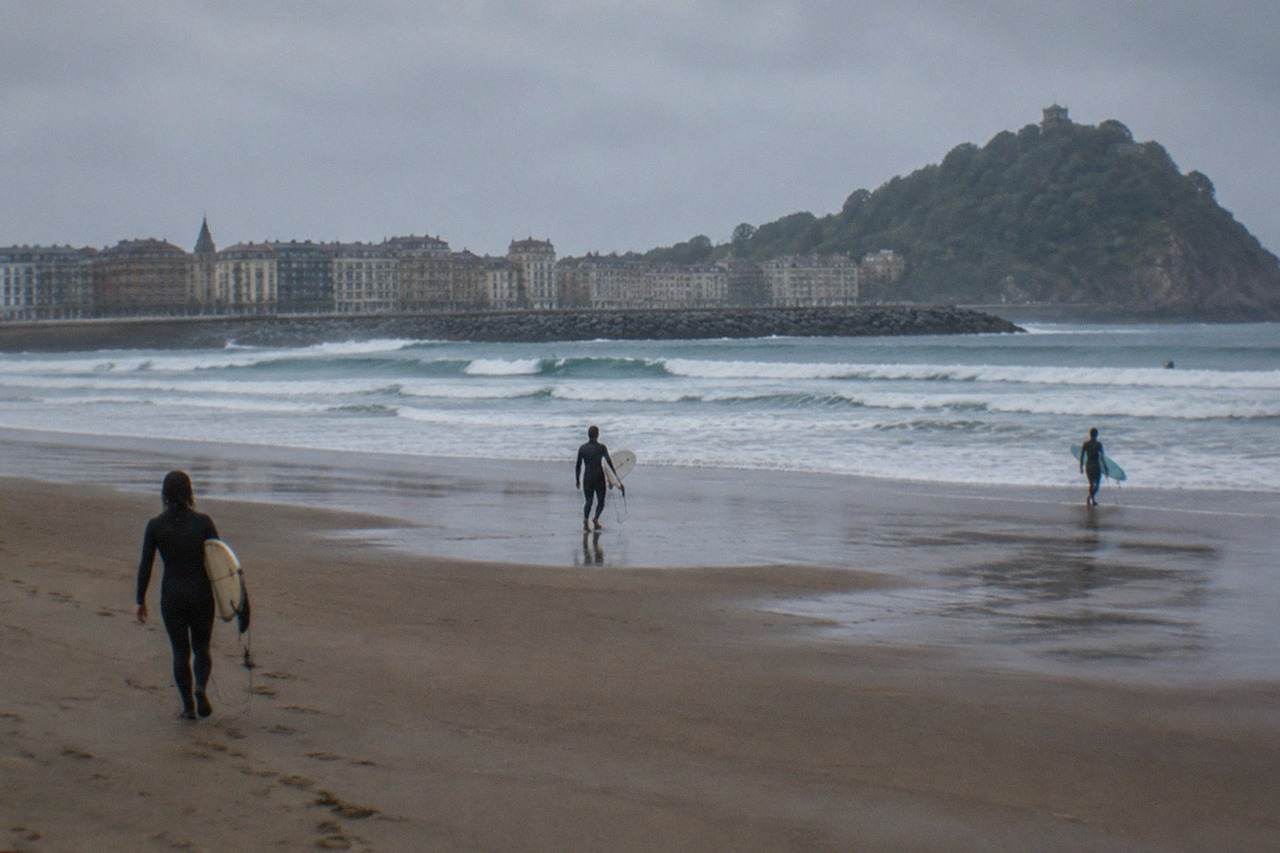 Surfers walking across the sandy Zurriola beach with the Gros seafront behind them