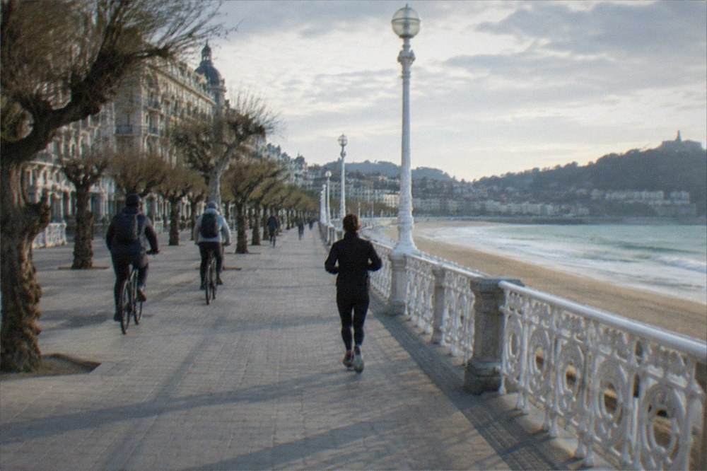 Cyclists riding along the flat seafront promenade beside Zurriola beach