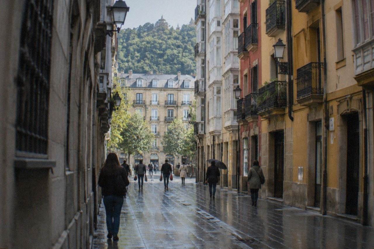 Narrow street in the old town with tall buildings, bar awnings and people strolling in the evening