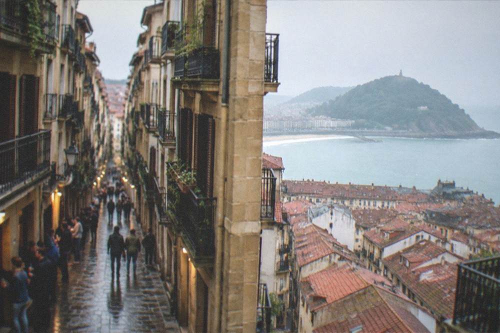 Evening view over red-tiled rooftops of the old town toward the bay and a green hill