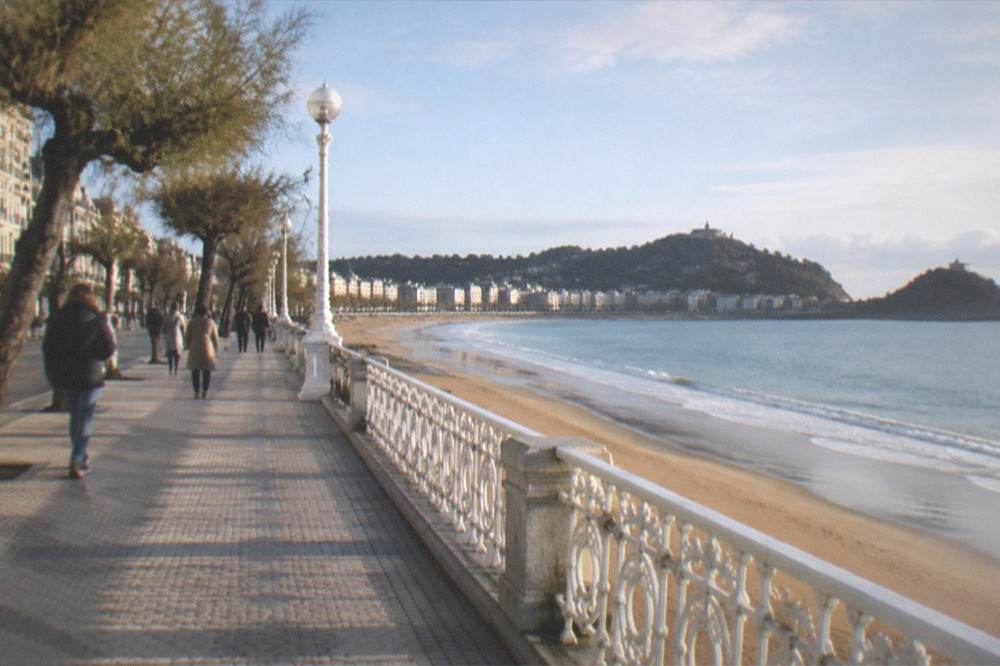 People walking along the La Concha promenade in San Sebastián between the beach and the belle époque buildings