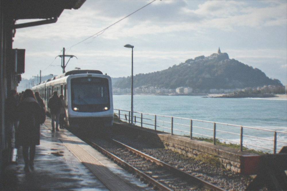 A narrow-gauge train arriving at a small station beside a bay