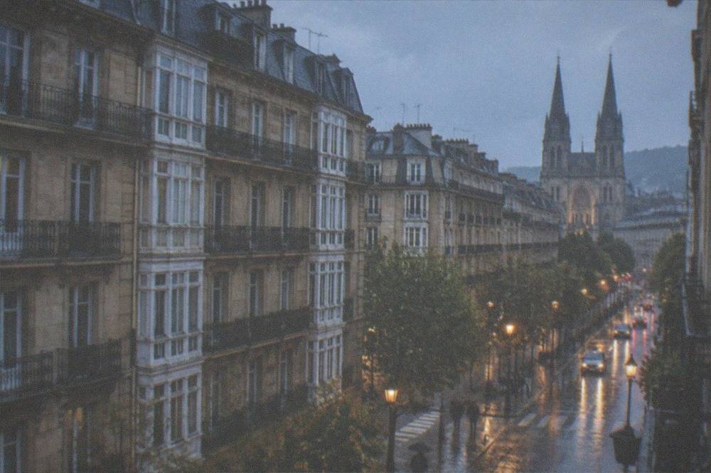 The cathedral towers seen through light rain from a Centro street corner with wet paving reflecting the stone.