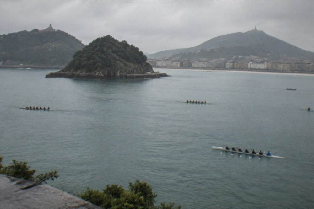 Rowing teams training on La Concha bay with the island and Monte Igueldo in the background.