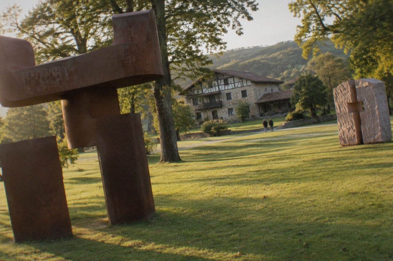 Large abstract steel sculptures standing on a mown lawn among trees at Chillida Leku