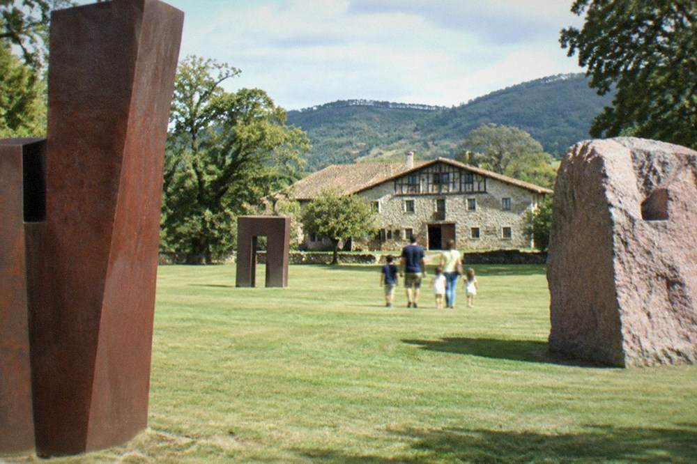 A family walking between tall abstract sculptures on the museum lawn at Chillida Leku