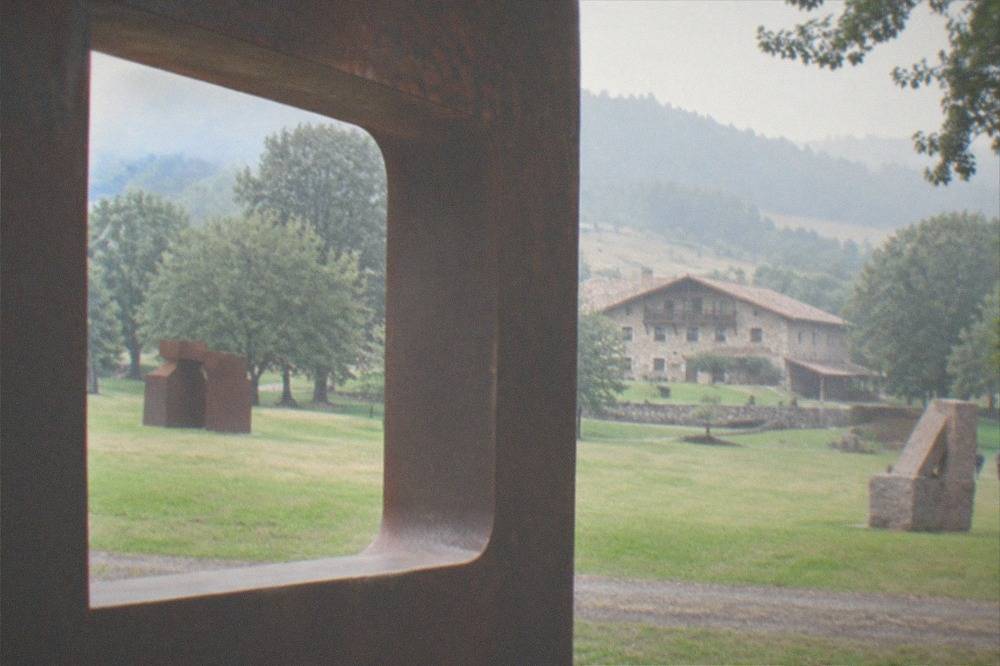 A rust coloured corten steel sculpture with an opening framing trees at Chillida Leku