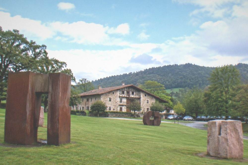 Cars parked in a woodland car park beside a lawn with large sculptures at Chillida Leku