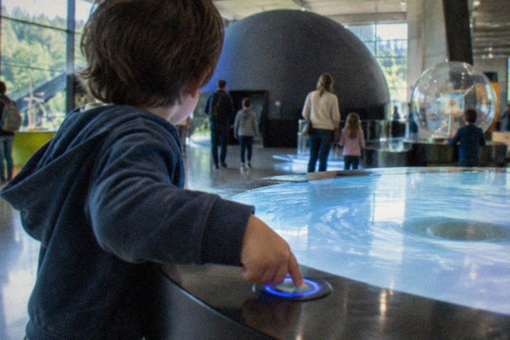 A child pressing a button on a glowing interactive display in a science museum