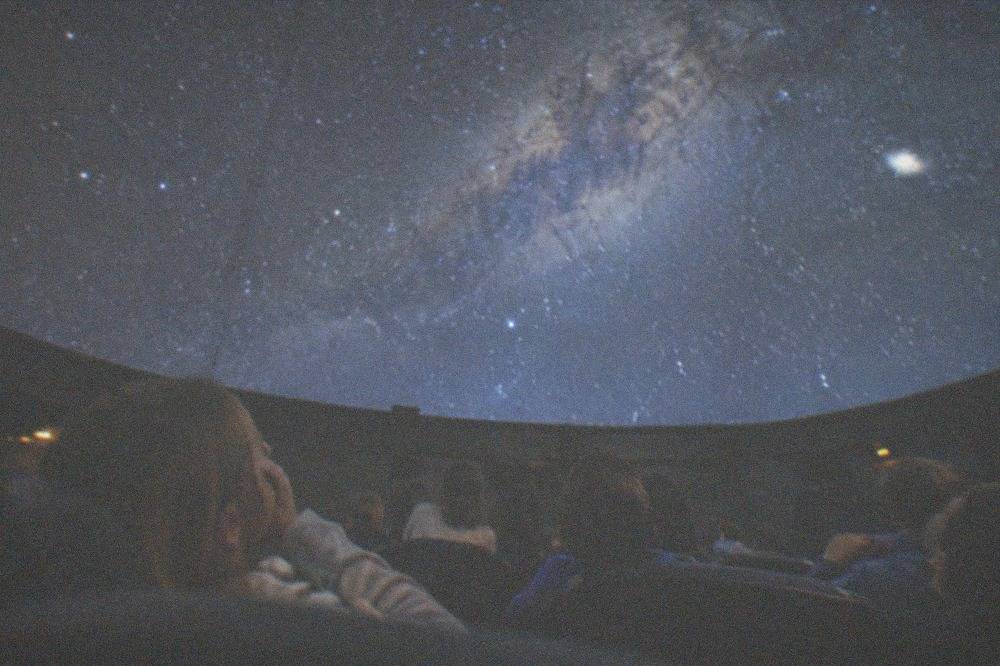 Children looking up at a domed planetarium ceiling filled with stars
