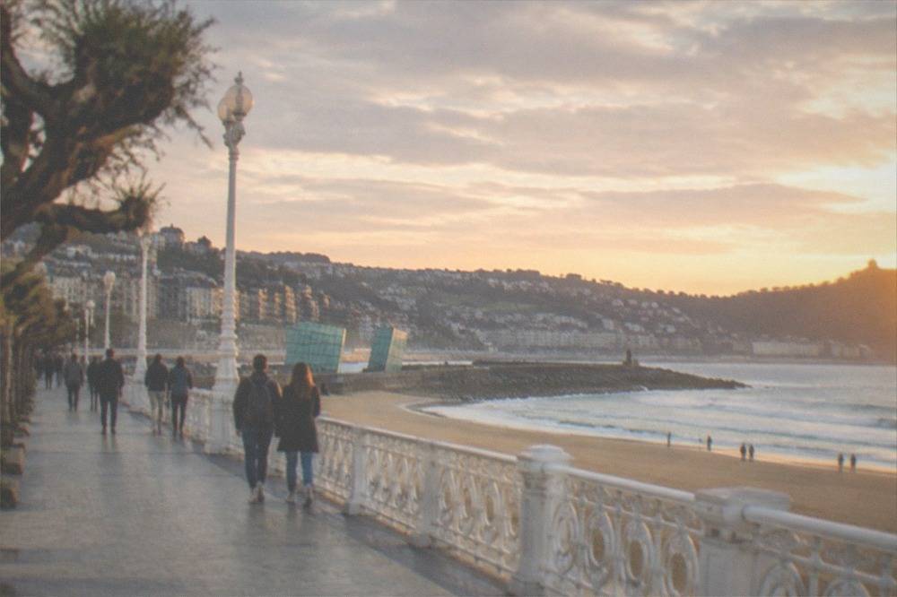Walkers on the Gros seafront promenade with the Kursaal cubes behind them and Zurriola beach to the right