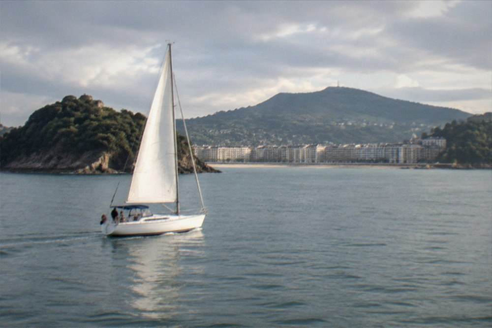A sailboat crossing La Concha bay with the city and hills behind