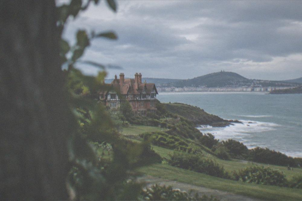 Waves breaking along the seafront near the palace headland under an overcast Atlantic sky