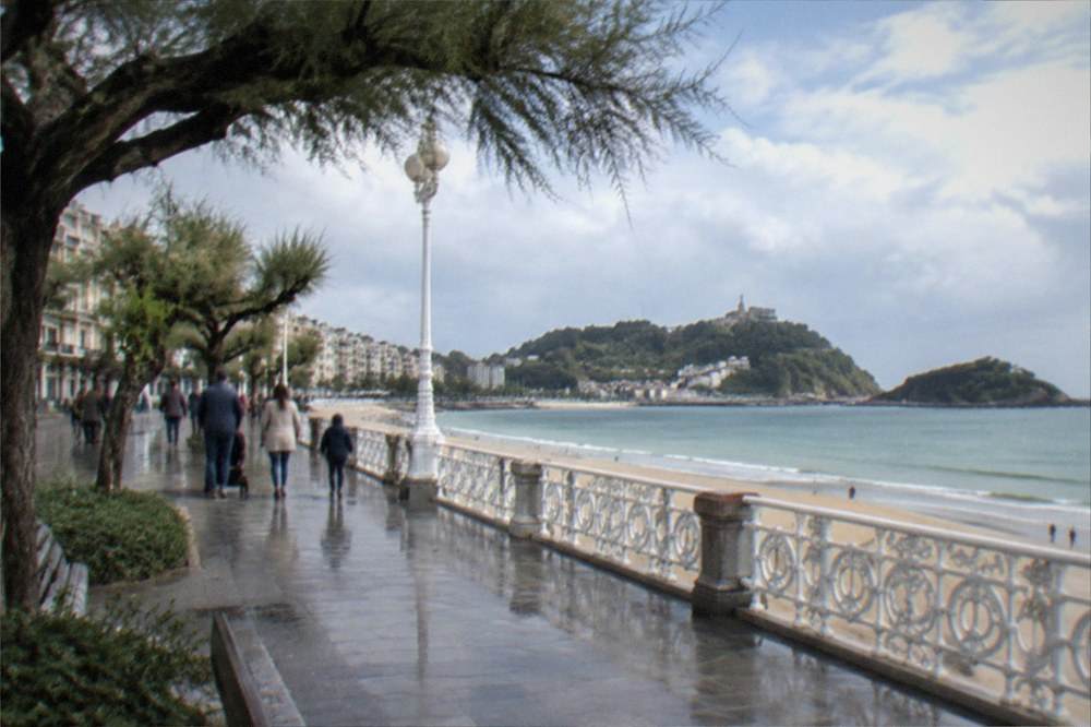 Families walking the flat promenade between La Concha beach and the palace headland