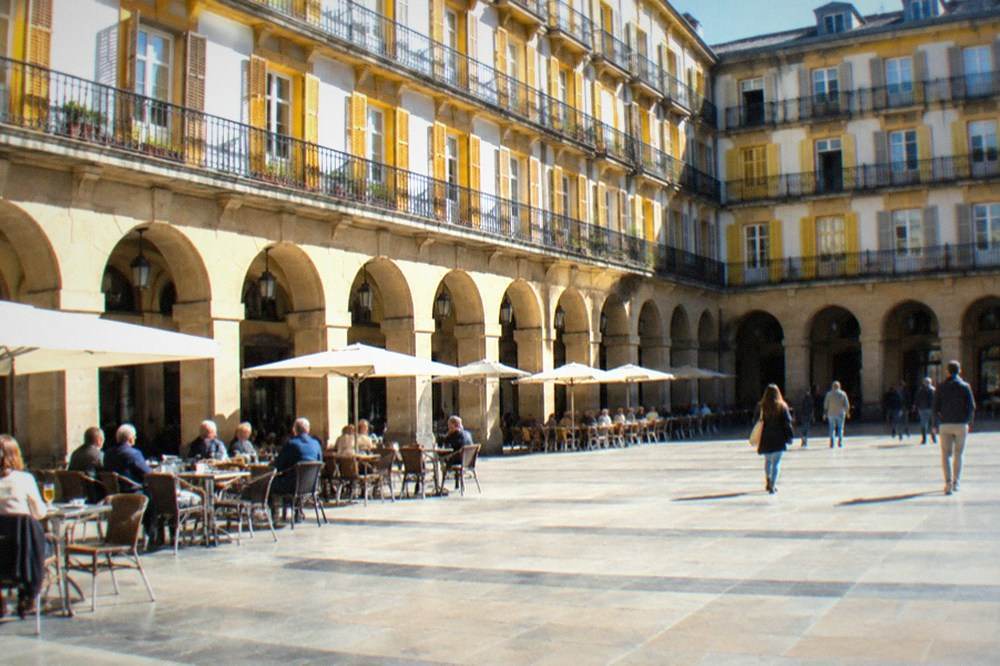 Cafe tables under the arcades of the Plaza de la Constitucion on a sunny morning