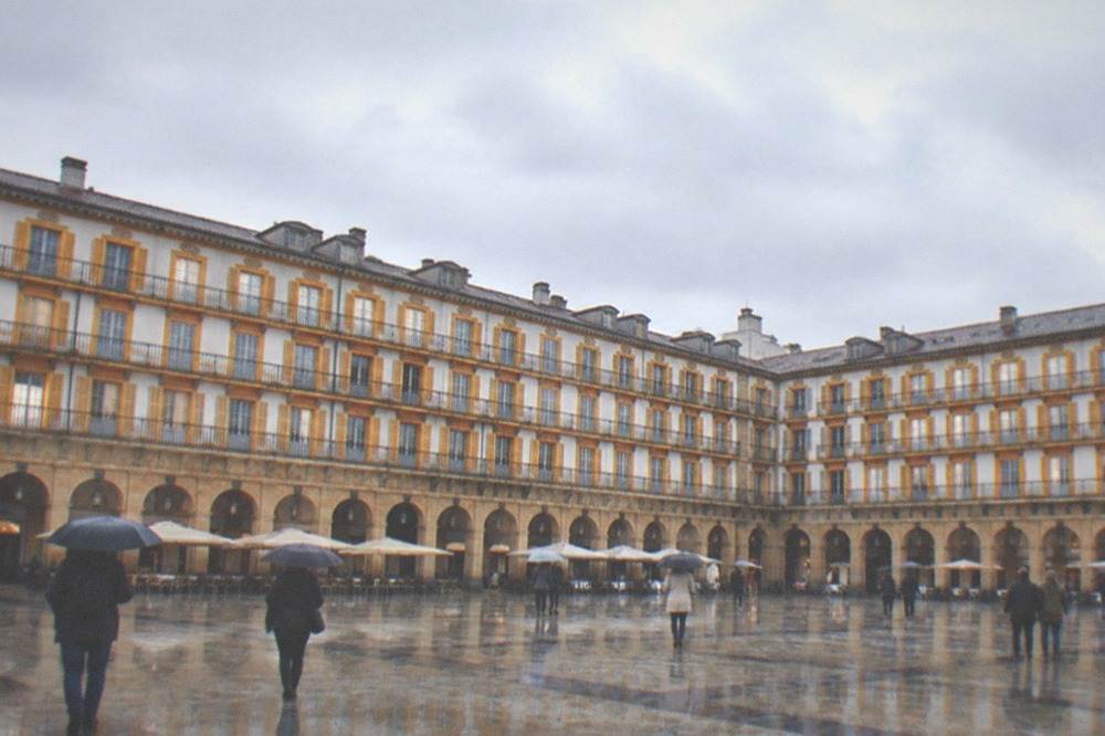 People walking across the Plaza de la Constitucion under overcast Atlantic skies