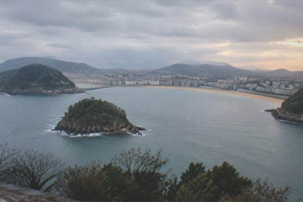 The full curve of La Concha bay seen from the high ground of the island at golden hour