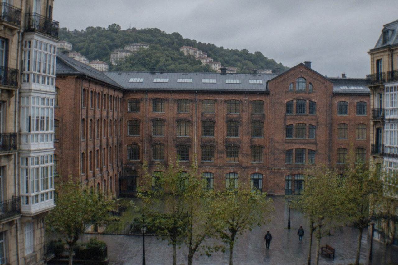 The courtyard facade of a large brick former factory building in San Sebastián under a cloudy sky
